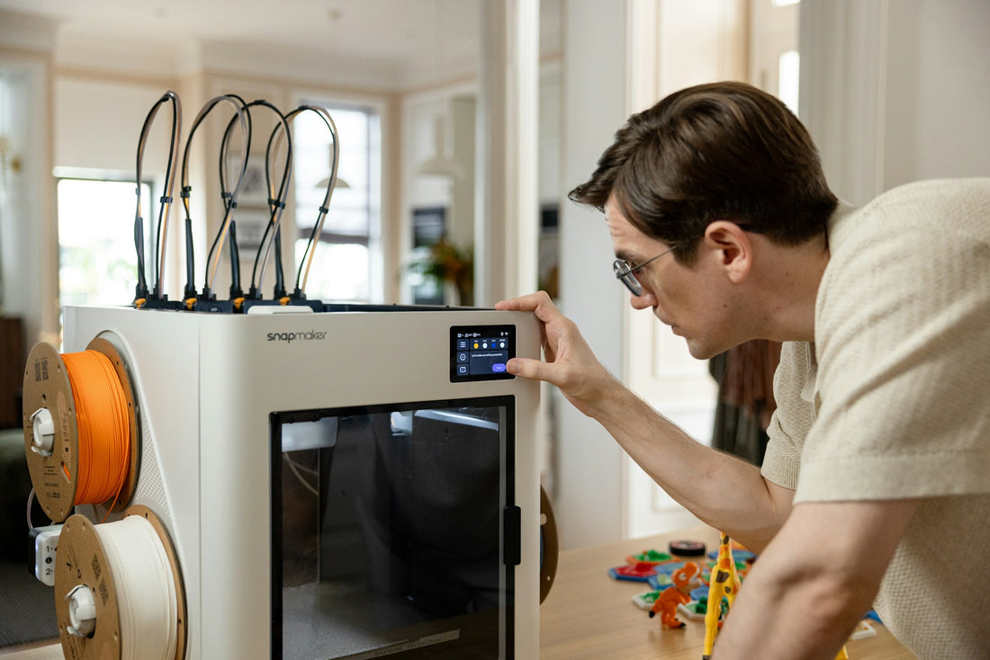 A maker adjusting a desktop 3D printer beside filament spools