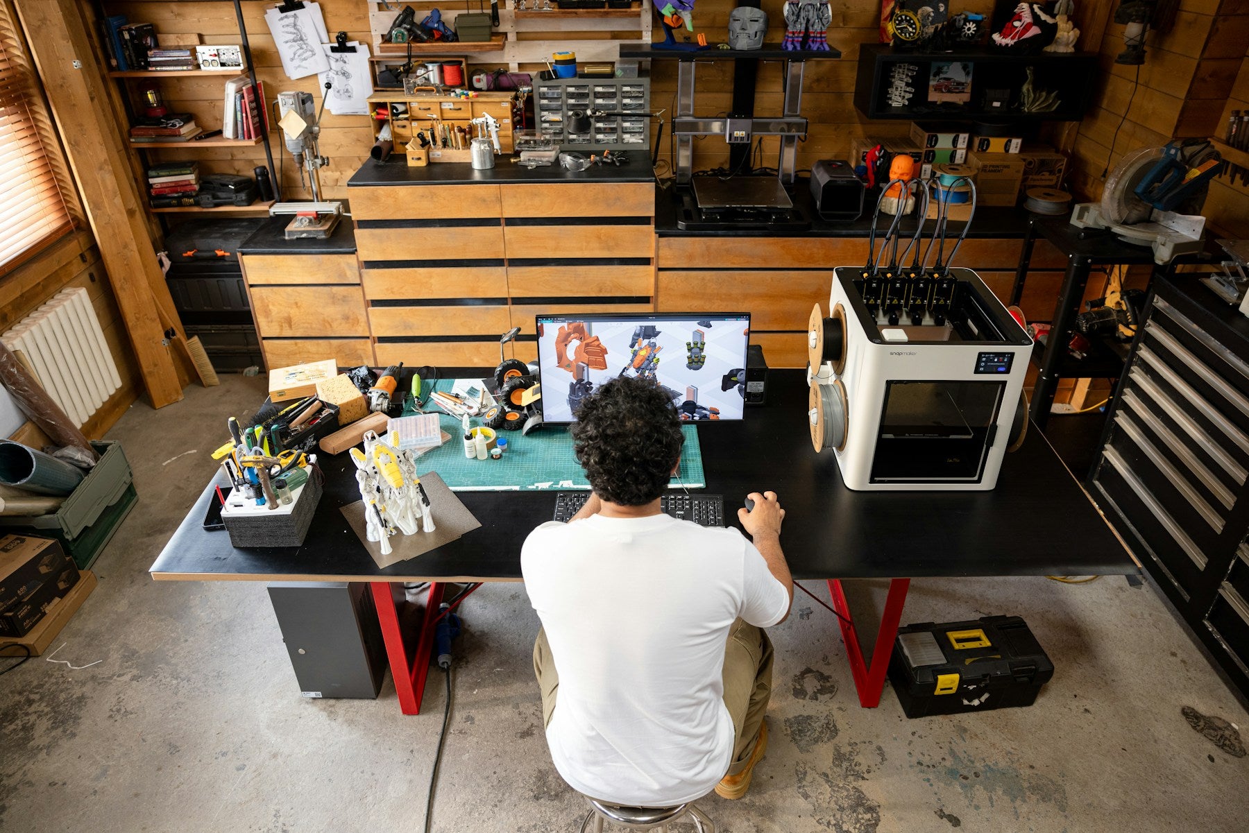 Maker working at a desk with a 3D printer and computer